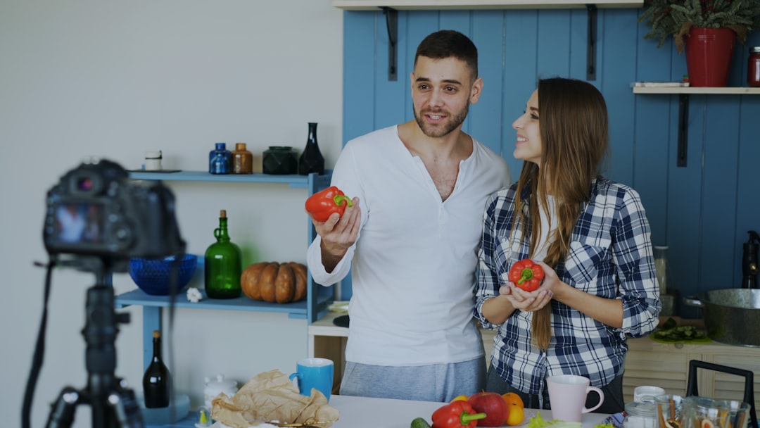 Young attractive couple recording video food blog about cooking on dslr camera in the kitchen at home