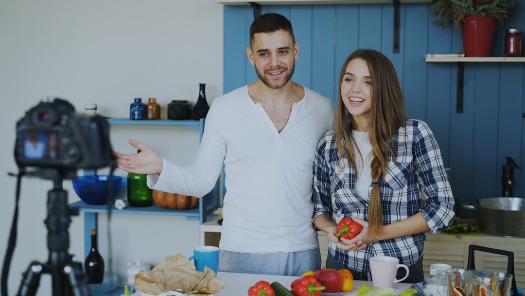 Young attractive couple recording video blog about vegetarian healthy food on dslr camera in the kitchen at home