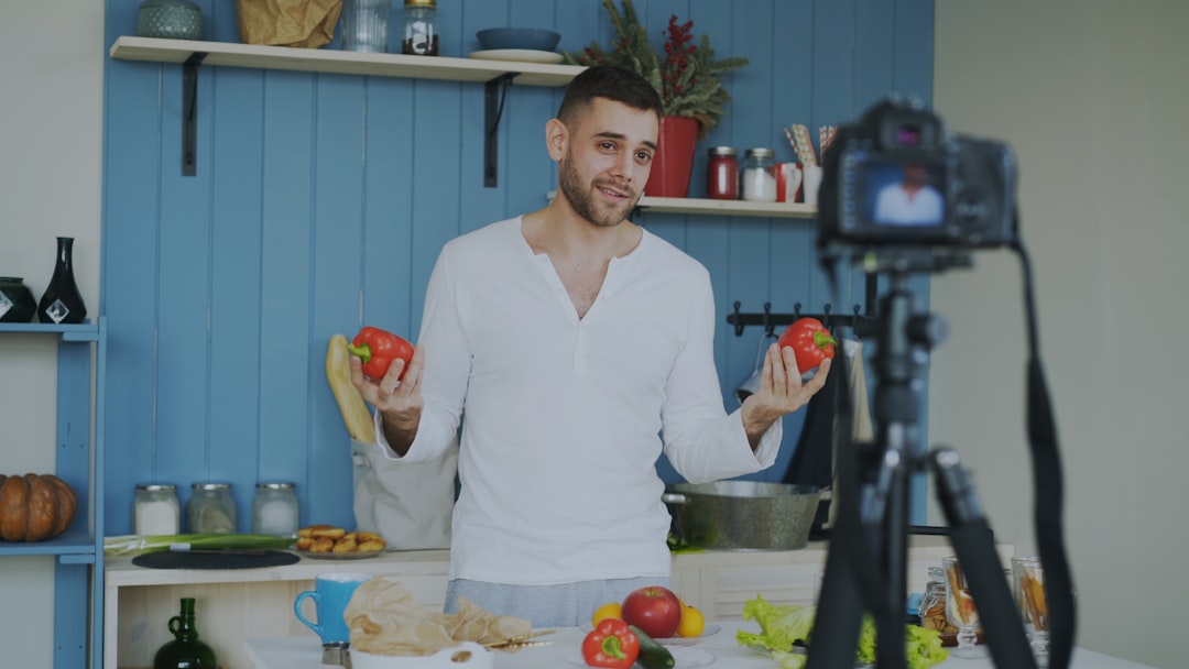 process-img Attractive cheerful man recording video blog about vegetarian healthy food on dslr camera in kitchen at home