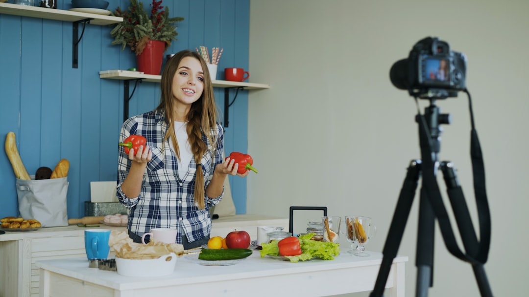 about-02 Young attractive woman recording video blog about vegetarian healthy food on dslr camera in kitchen at home