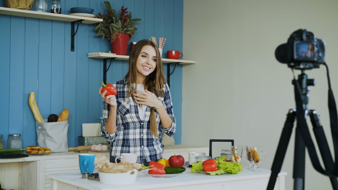 awards-img Young attractive woman recording video blog about vegetarian healthy food on dslr camera in kitchen at home